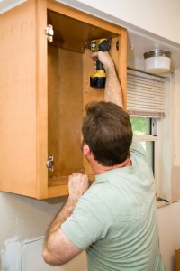 Carpenter screwing solid maple cabinets into the wall. 